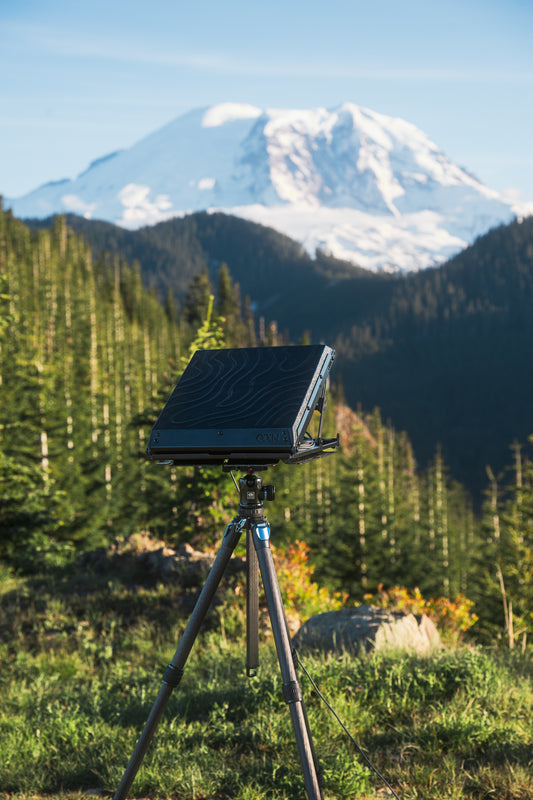 Tuff Mount for Starlink Mini shown on a Tripod using the Tripod Adapter in the wilderness with mountain in the background. 